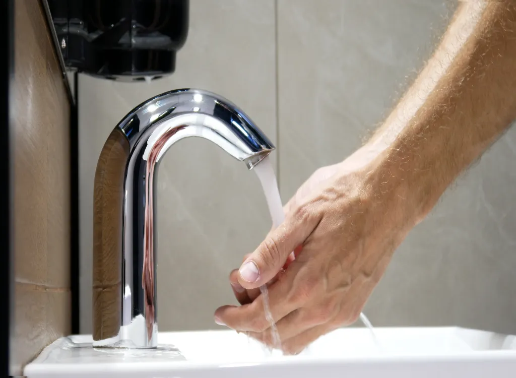 A man washes his hands using a touchless smart faucet, one of the best kitchen appliances of 2022.