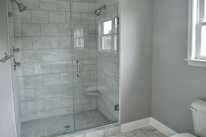 Shower with two shower heads and glass doors gray tiles for sleek modern look