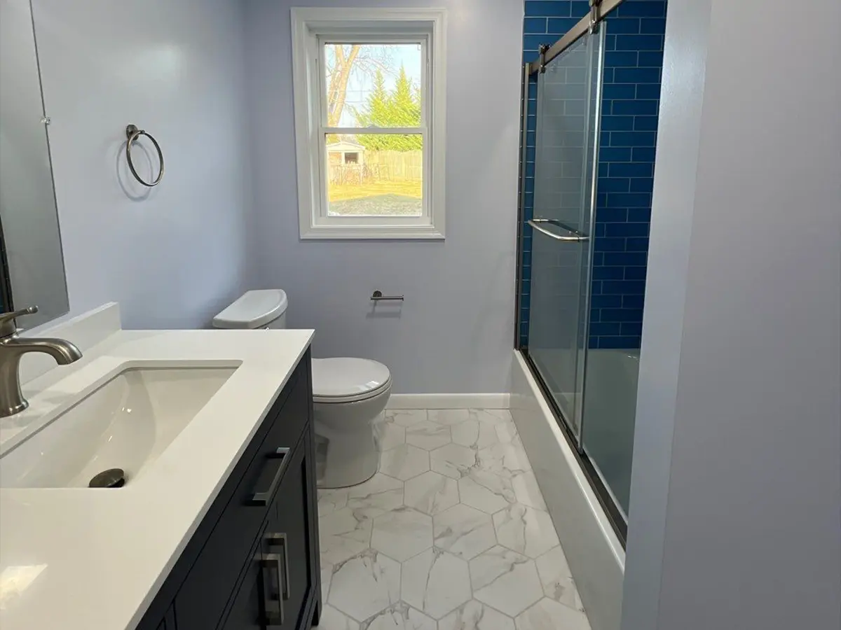 Bright remodeled bathroom with blue tile shower and white vanity
