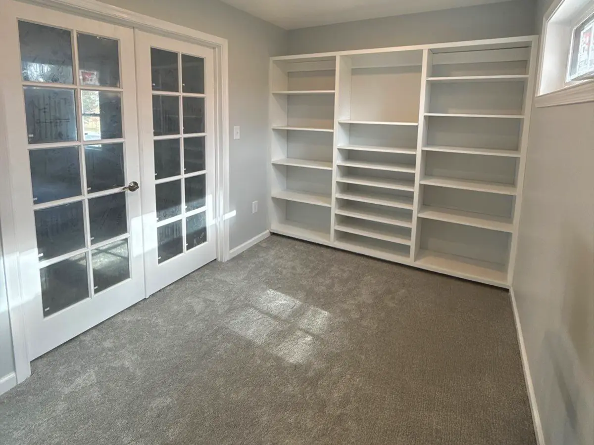 Finished home office with carpet flooring and built-in white bookshelves