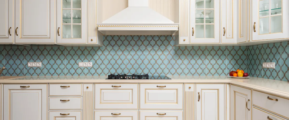 Traditional kitchen with cream cabinets, gold trim, and aqua tile backsplash.