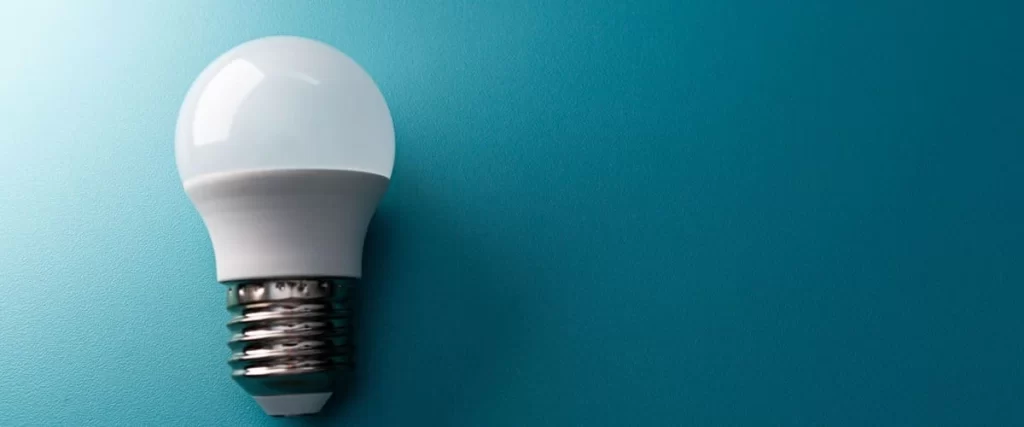 A modern white LED daylight spectrum bulb positioned on the left side against a vibrant teal textured background with soft lighting and ample copy space on the right.