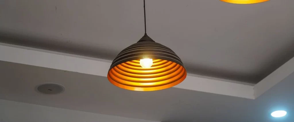 A close-up shot of modern industrial pendant lights featuring a ribbed matte black exterior and a warm glowing gold-leaf interior hanging from a white ceiling.
