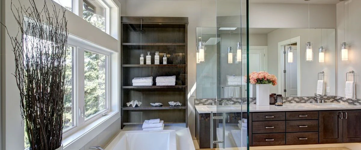 A spacious luxury bathroom showcasing a dark wood double vanity with white countertops, a large glass-enclosed shower, a soaking tub positioned next to floor-to-ceiling windows, and elegant pendant lighting.