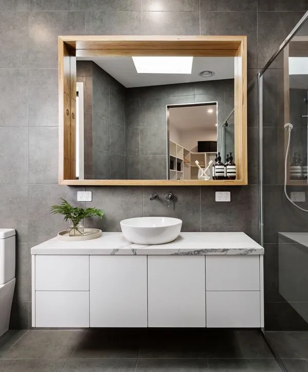A modern bathroom remodeling project in Lake Shore, MD, featuring a floating white vanity with a marble countertop, vessel sink, and a large wood-framed mirror against grey tiles.