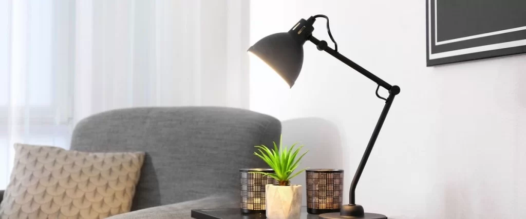 A sleek black adjustable swing arm table lamp illuminating a cozy living room setup with a small potted succulent and decorative candle holders on a dark side table.