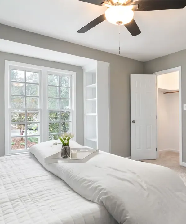 A sunlit primary bedroom with white bedding, large windows, and an integrated closet following a professional home remodeling in Millersville, MD.