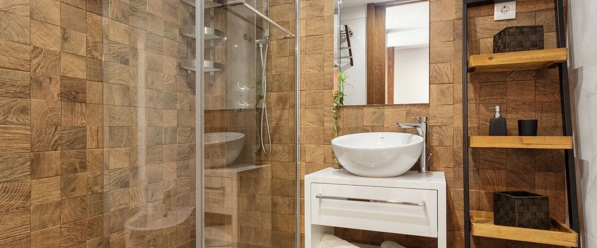 A contemporary bathroom interior showing a textured wood-block accent wall, a white vessel sink vanity, and a glass-enclosed walk-in shower.
