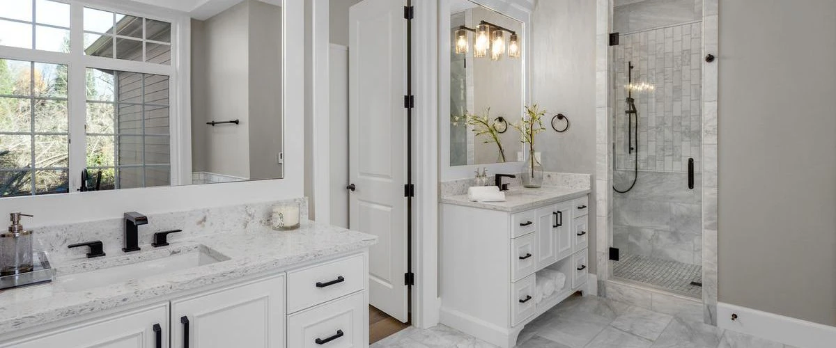 Interior view of a contemporary bathroom with a white double sink vanity, black hardware, and a walk-in marble tile shower.