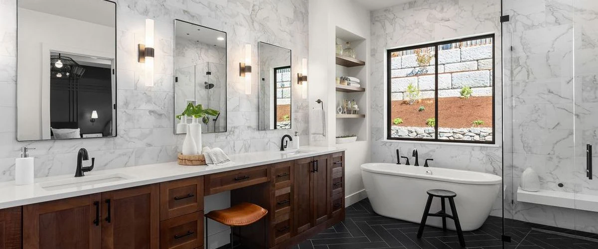Luxury bathroom design with white marble wall tiles, a freestanding oval bathtub, dark chevron wood floors, and a long dark wood double vanity.