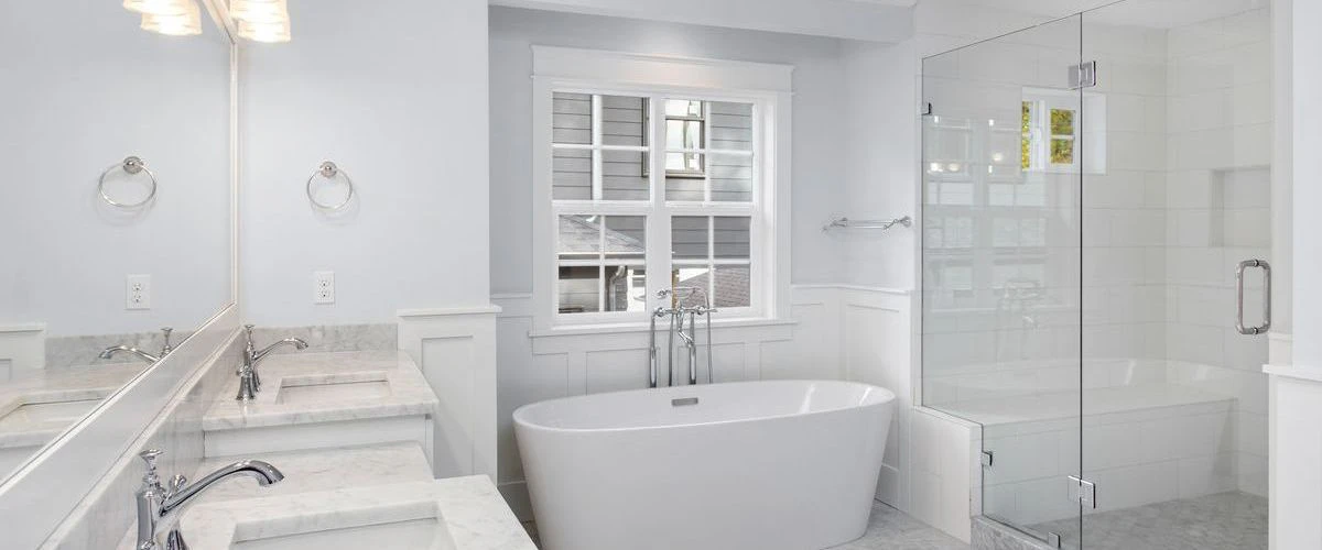 A bright and spacious white master bathroom showcasing a large soaking tub, marble double vanity, and a separate glass shower.