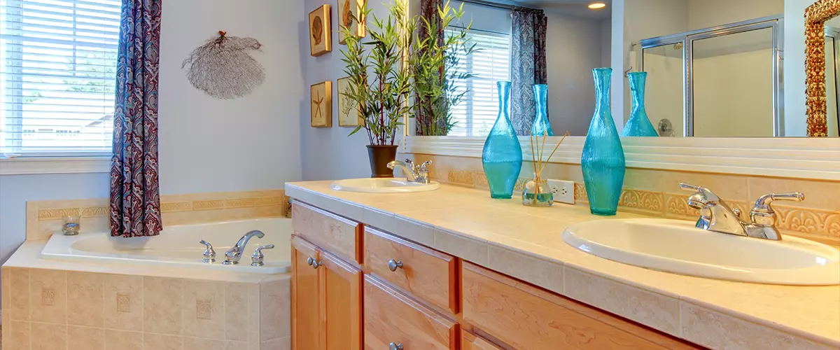 Traditional bathroom featuring a corner soaking tub, a dual sink vanity with oak cabinets, and bright blue decorative glass vases and curtains.