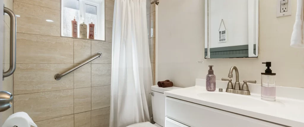 Bathroom accessibility for seniors featuring wall-mounted stainless steel safety grab bars in a tiled shower area next to a white accessible vanity.