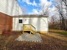 New white rear home addition with small wooden staircase and brick paver patio