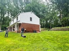 Two workers preparing the yard beside a two-story white and red brick home