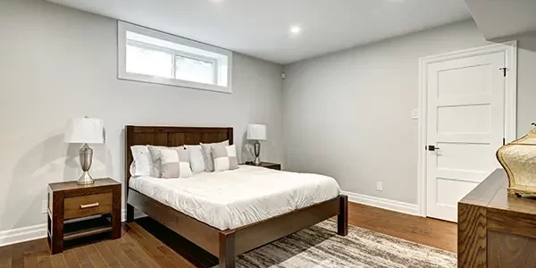 Modern basement bedroom with wood flooring, recessed lighting, and platform bed beneath egress window Modern basement bedroom with wood flooring, recessed lighting, and platform bed beneath egress window